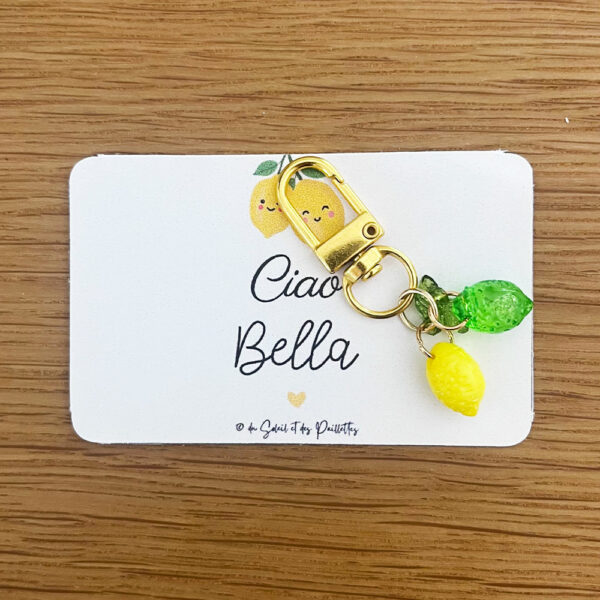 Grigri de sac et porte-clé citron jaune solaire posé sur sa mini-carte cadeau au message complice Ciao Bella.
